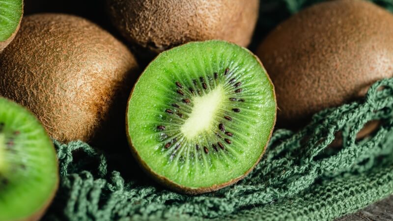 Owoc kiwi w całości i przekrojony na pół z widocznym zielonym miąższem