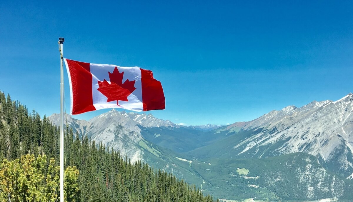 Flaga Kanady z czerwonym liściem klonu powiewająca na tle majestatycznych górskich szczytów i lasów iglastych