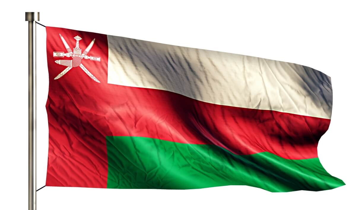 Flaga Omanu z charakterystycznym herbem z mieczami na czerwono-biało-zielonych pasach powiewająca na wietrze