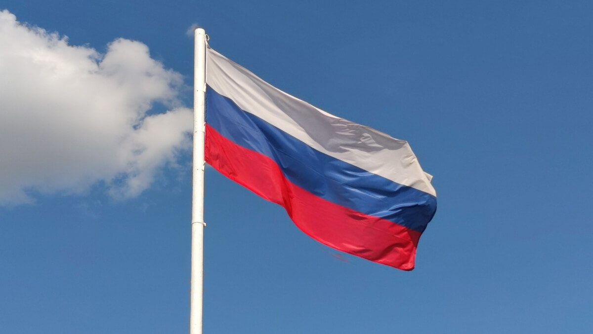 Flaga Rosji z białymi, niebieskimi i czerwonymi pasami powiewająca na tle błękitnego nieba z chmurami