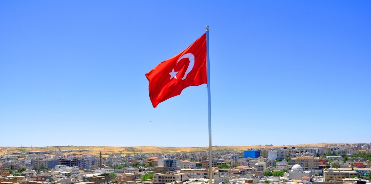 Flaga Turcji z białą gwiazdą i półksiężycem na czerwonym tle powiewająca nad panoramą tureckiego miasta