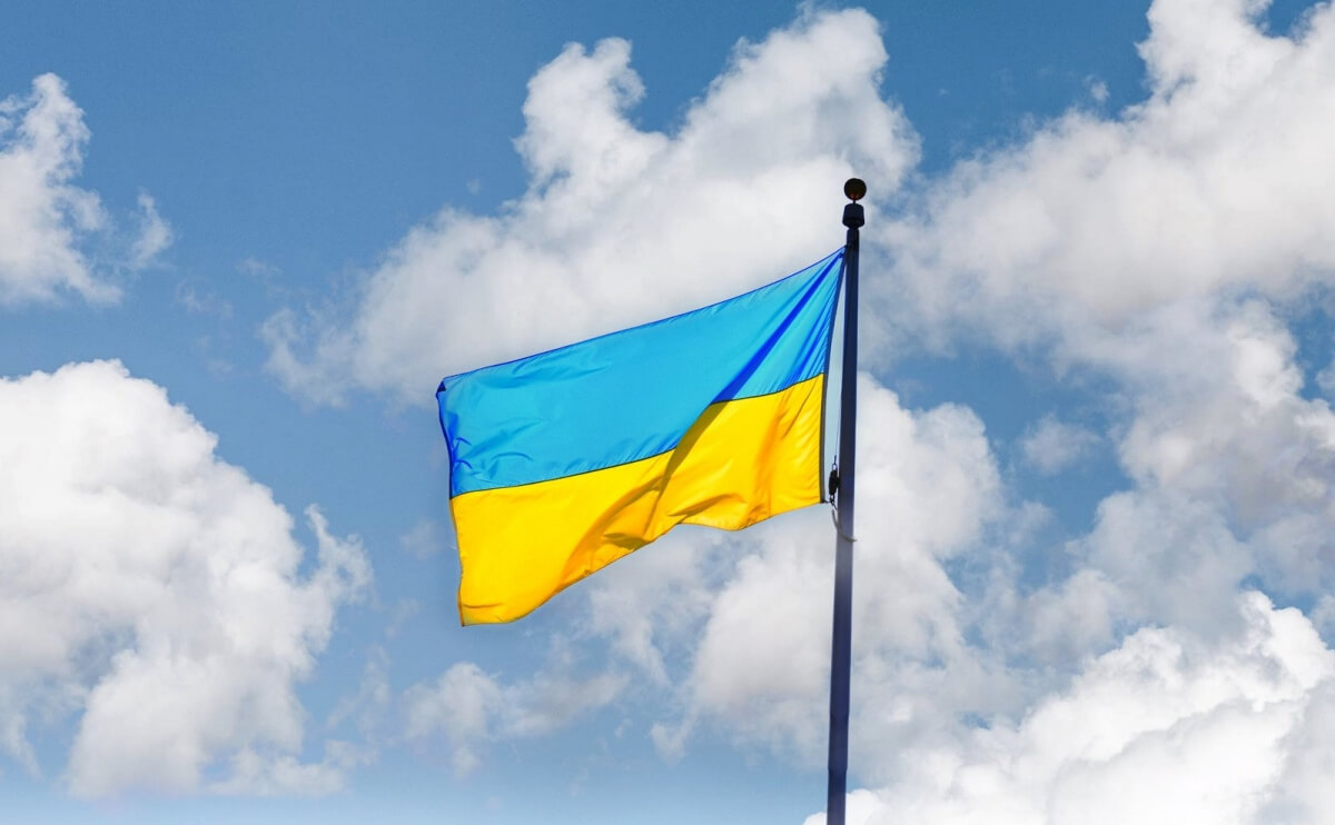Flaga Ukrainy z niebieskim i żółtym pasem powiewająca na tle błękitnego nieba z białymi chmurami