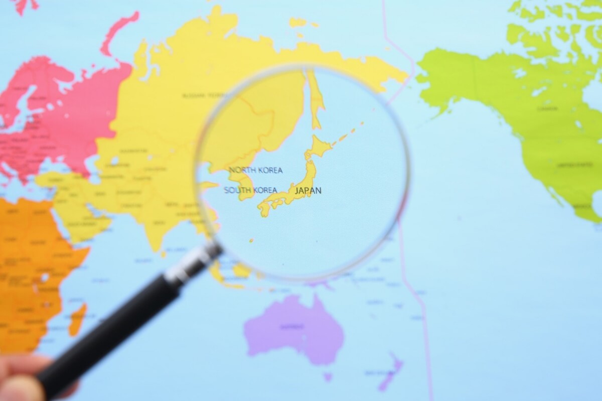 Mapa świata z lupą powiększającą Japonię, Koreę Południową i Północną na tle kolorowej mapy